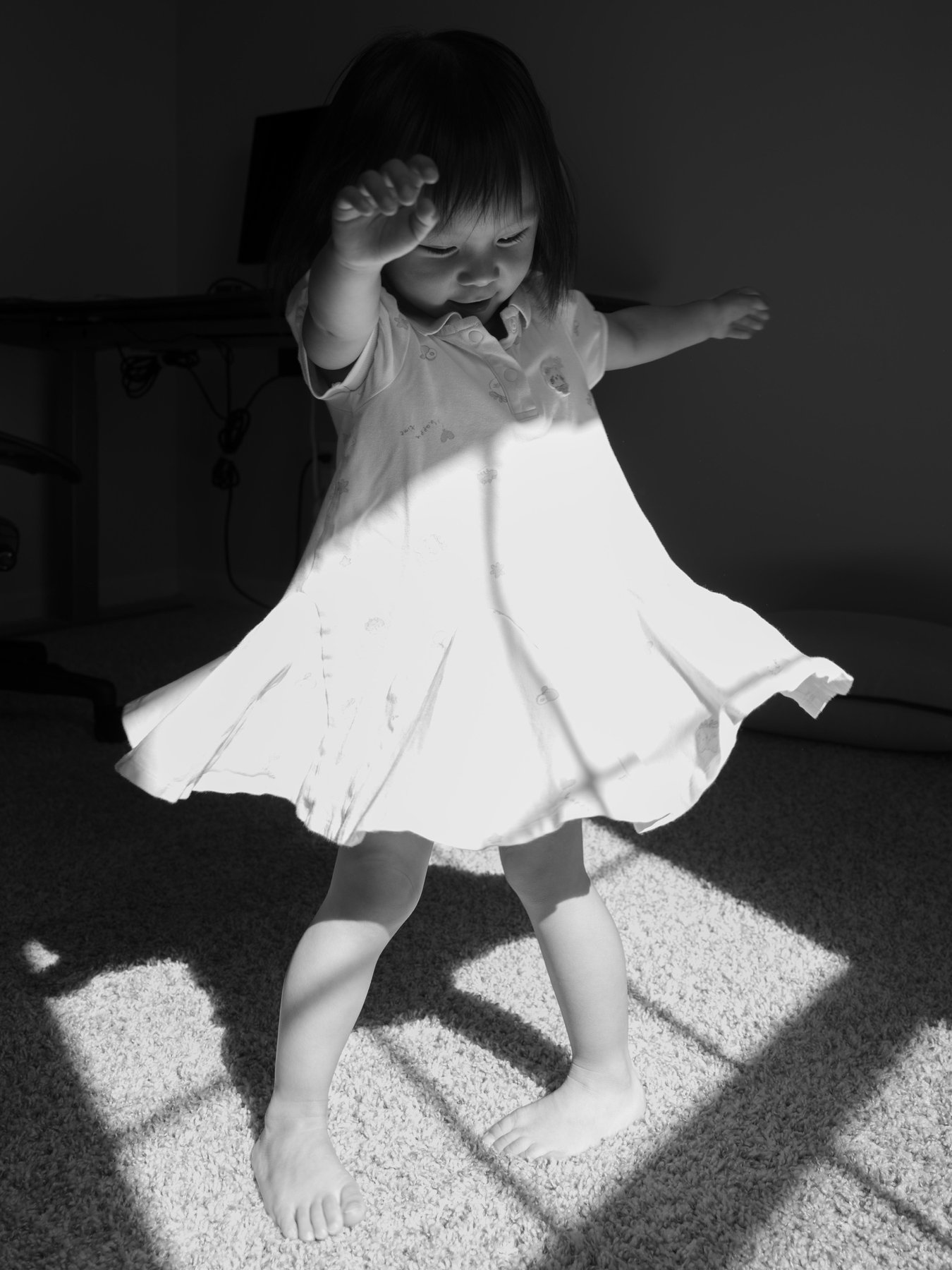 Child twirling in a sunlit dress, black and white