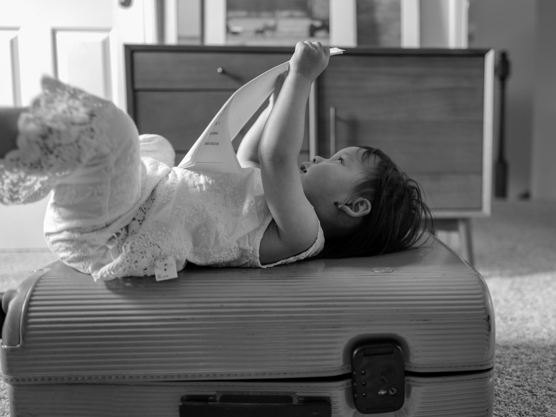 Child lying on a suitcase reading, black and white