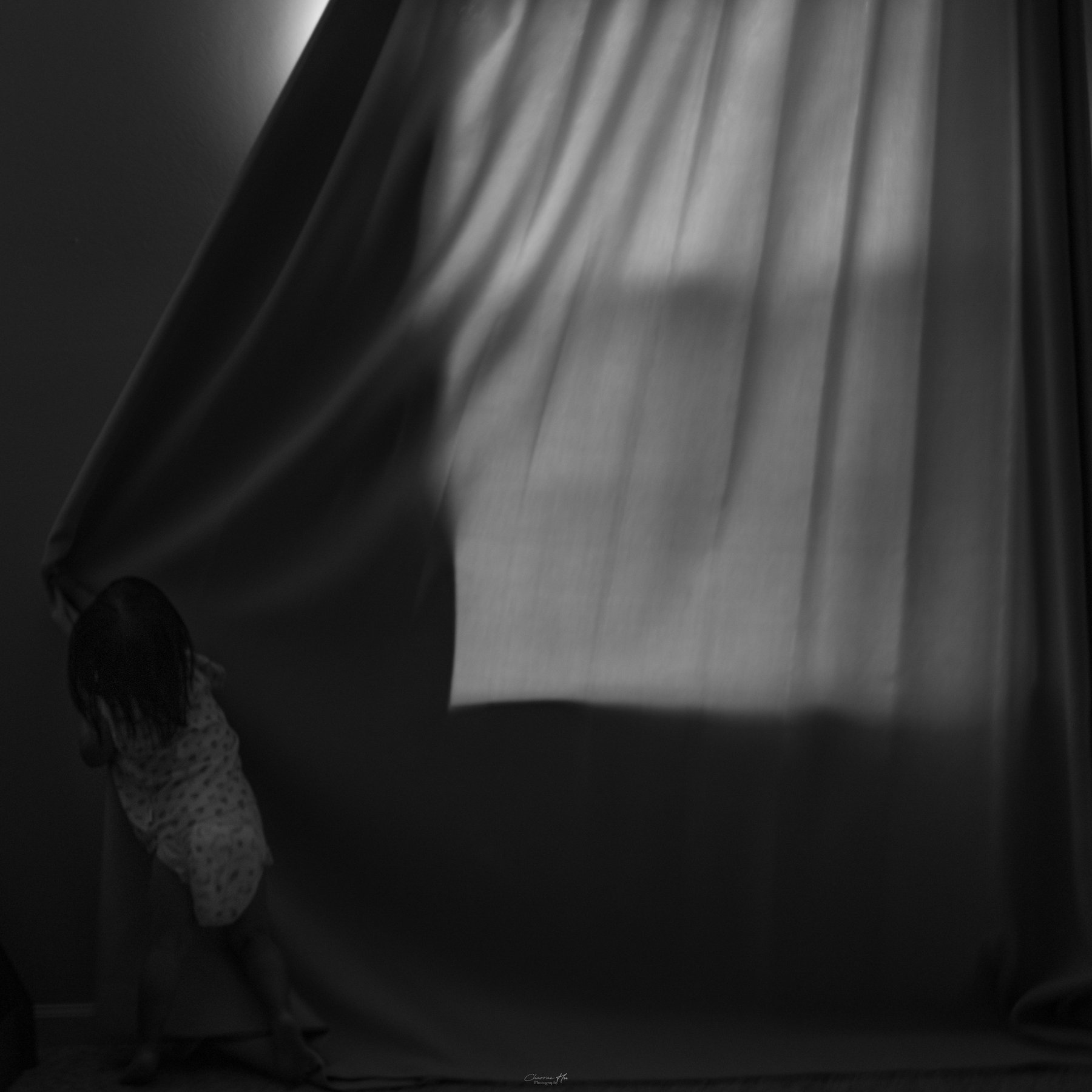 Child pulling a curtain in a dark room, black and white