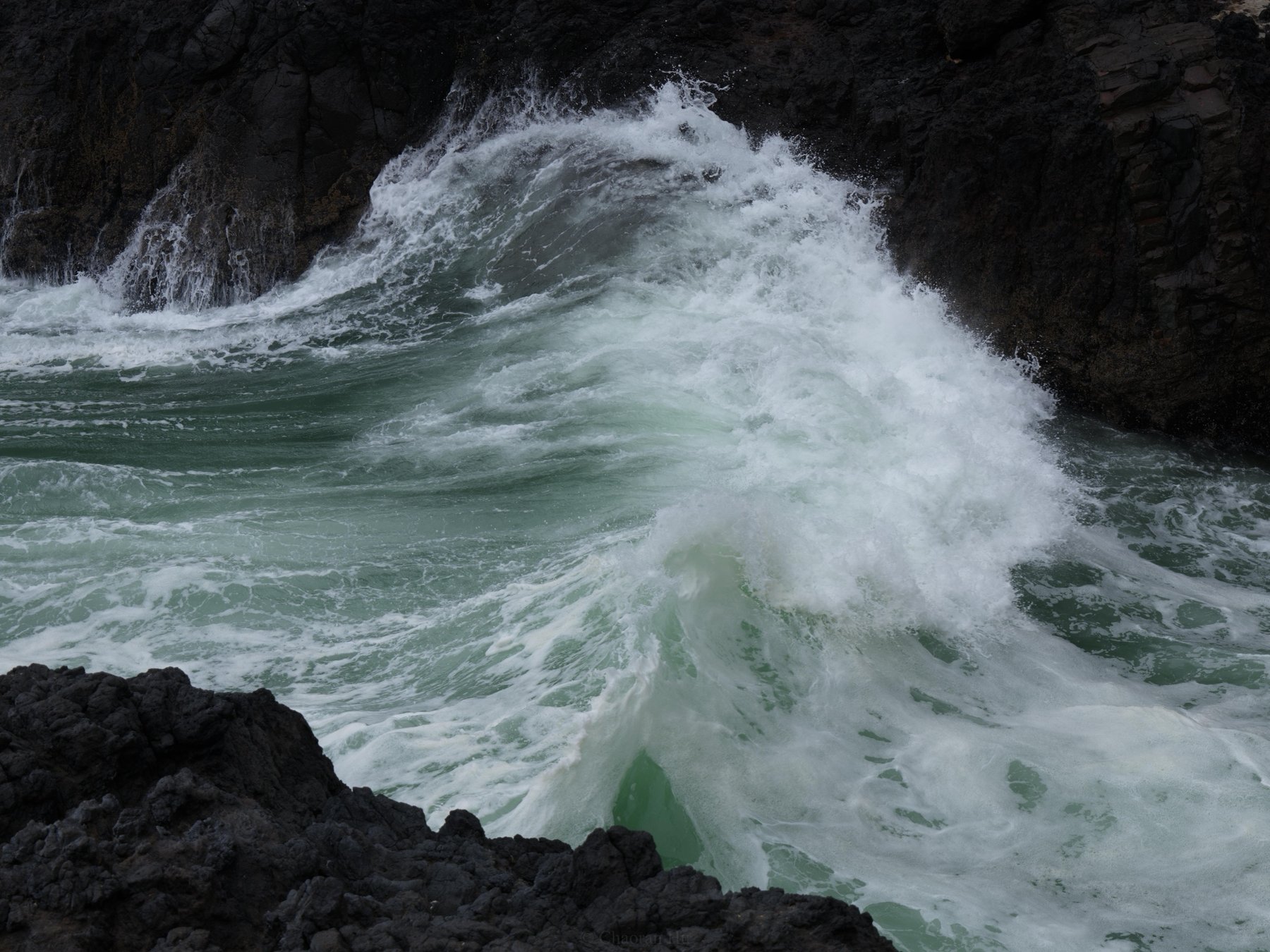 Wave breaking against dark rocks